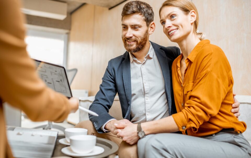 Young couple discussing real estate options with a consultant, seated with coffee cups, in a modern office setting.