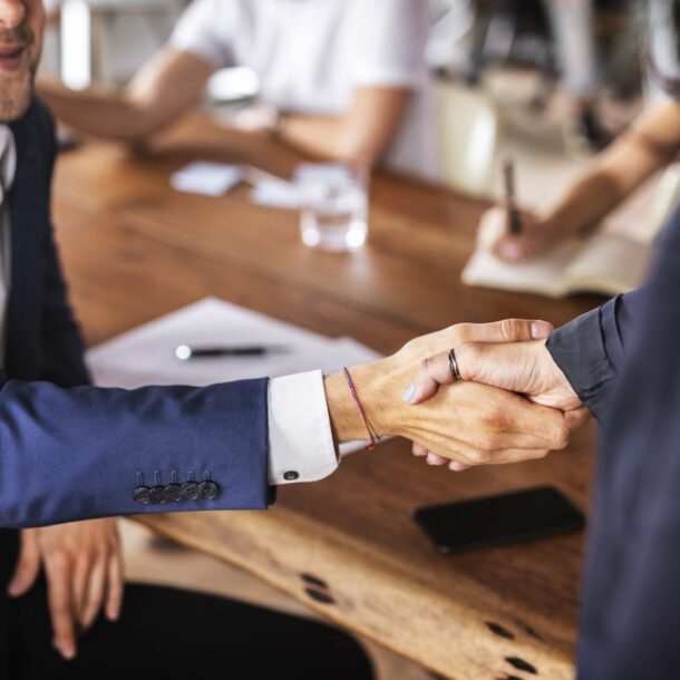 Business professionals shaking hands in a collaborative office setting, symbolizing legal partnerships and assistance of counsel at Abrahams Solicitors.