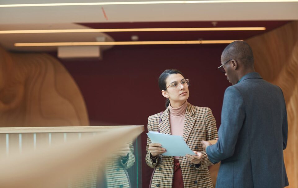 Businesswoman consulting with businessman in modern office setting, discussing legal documents, relevant to Abrahams Solicitors' legal services.
