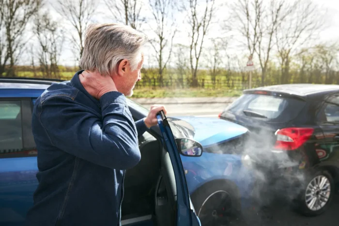 Man holding his neck after a car accident, with damaged vehicles in the background, illustrating personal injury claims related to car accidents.